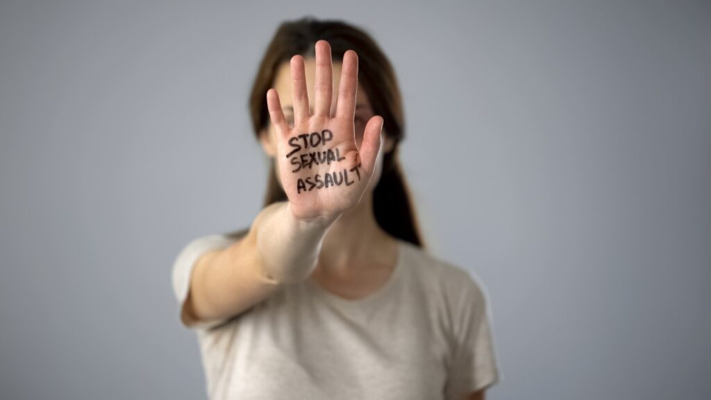 A photo of a young woman has her hand raised to the camera to cover her face. On her palm reads the words, "Stop Sexual Assault."