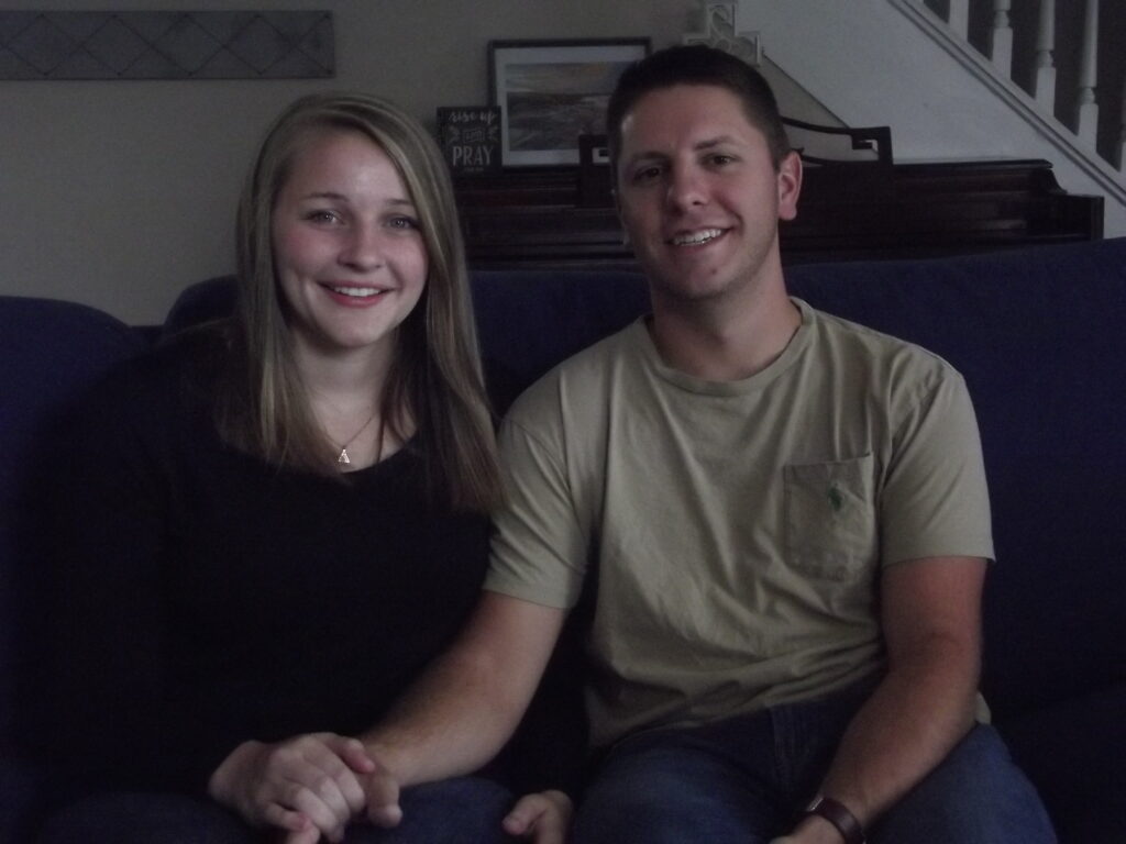 Two young people sit side-by-side on a couch.