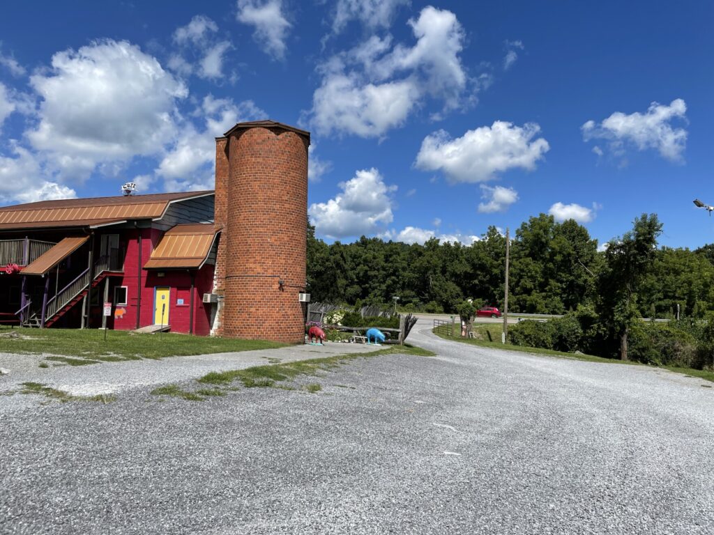 A brick building can be seen in the distance. Closer to the camera is a gravel path. The sky is blue with some white clouds.