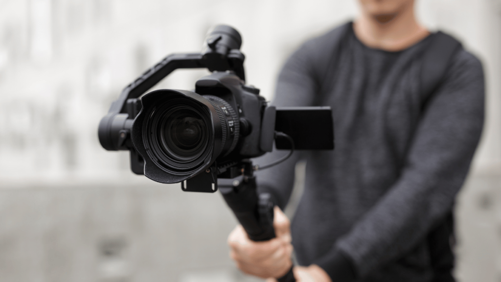 A filmmaker holds a camera on a tripod.