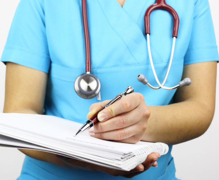 A nurse practitioner wearing a stethoscope and a blue uniform as she writes notes in a health ledger.