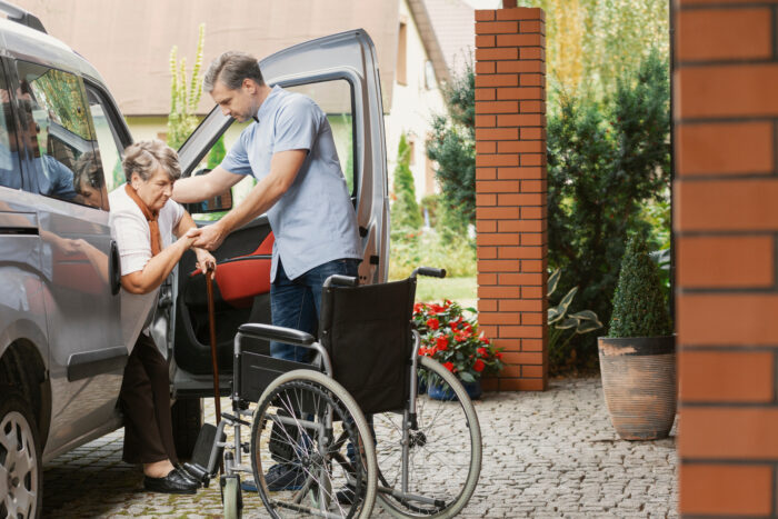 A man helps an elderly woman out of a vehicle.