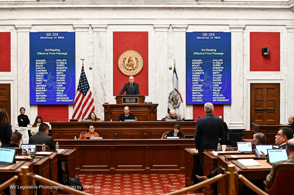 Sen. Mike Woelfel, D-Cabell, can be seen standing to address Senate President Craig Blair, R-Berkeley, during discussion of Senate Bill 268 Feb. 25, 2023. Blair is flanked on either side by blue screens displaying Senate Bill 268, titled "Relating to PEIA"
