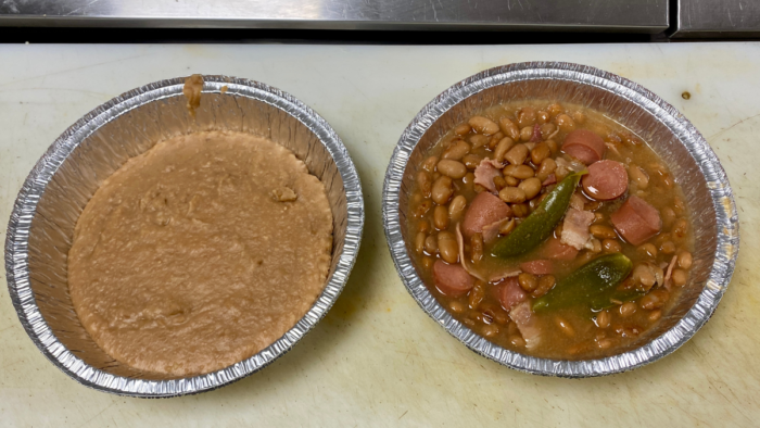 A bowl of frijoles charros sits to the right of a bowl of refried beans.