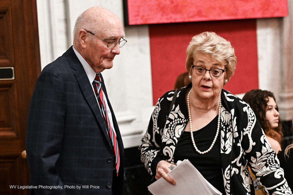 Sen. Donna Boley, R-Pleasants, stands next to Sen. Charles Clements, R-Wetzel, with a red backdrop on the Senate floor.