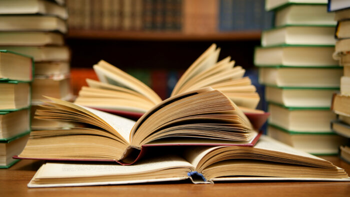 A stack of books on a table with two opened and their pages fanned out.