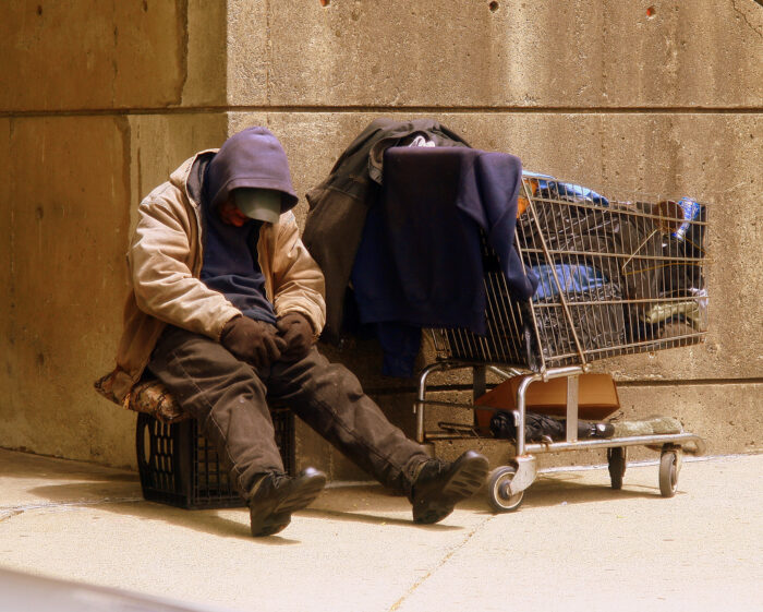 A homeless man sleeps next to a cart full of his possessions.