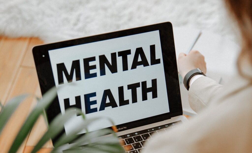 A tablet shows the words "Mental Health" as a person sits ready to read.