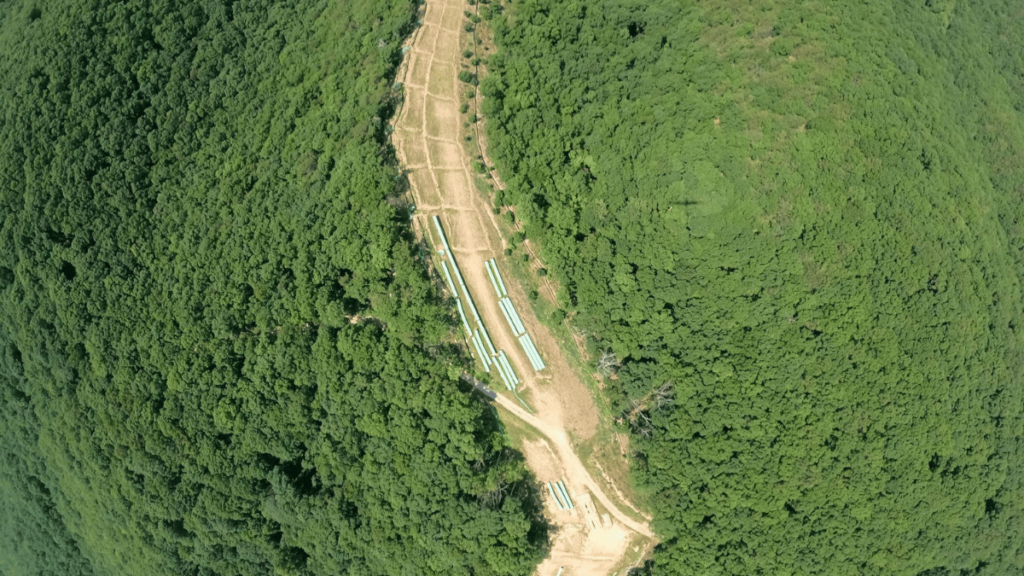 An aerial photo of the Mountain Valley Pipeline. The unfinished project is seen in a trench in the middle of a green forest.