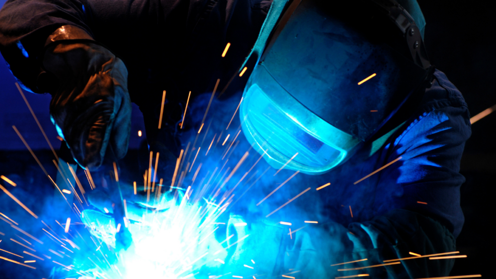 A welder wearing a safety helmet works with an arc welder as sparks fly.