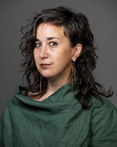 A professional headshot of a woman with dark hair wearing a dark green shirt.