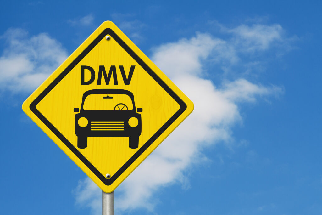 Warning Sign, Icon of a car with text that reads DMV on a yellow highway sign with sky background.