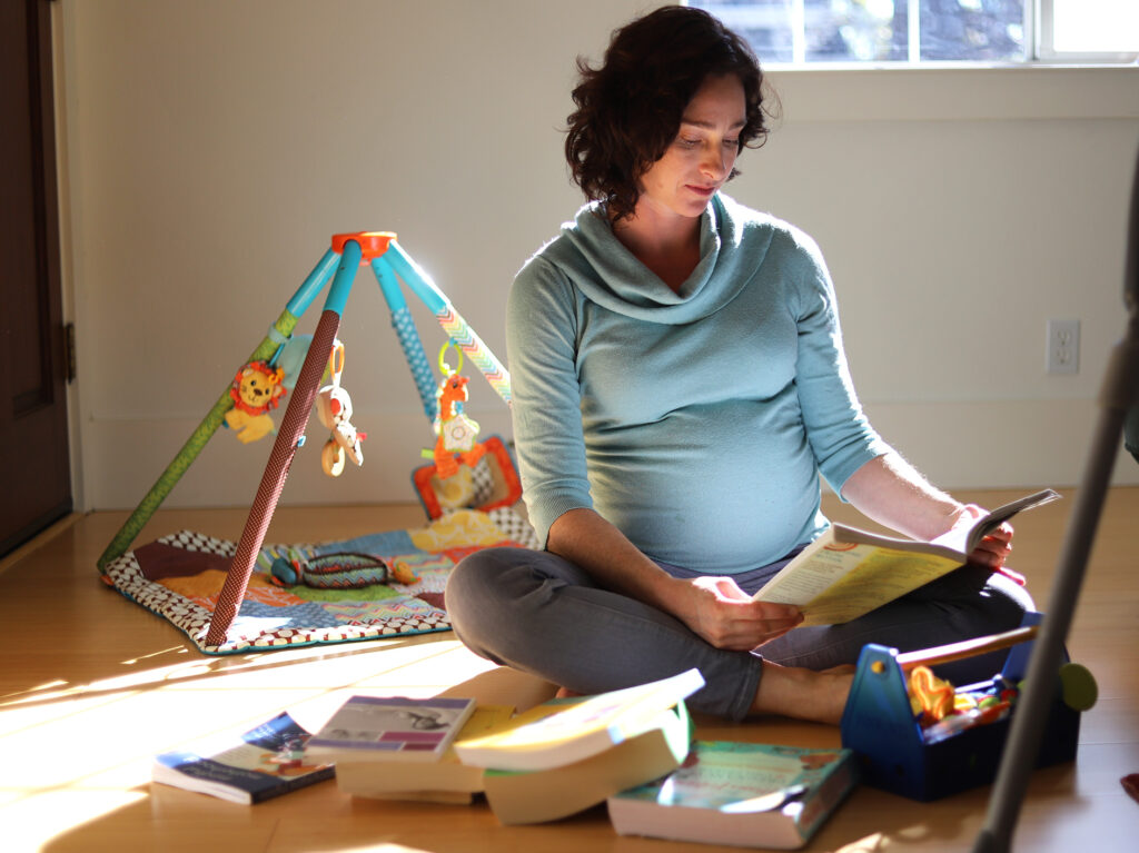 A woman sits on the floor of her home reading a birthing book.