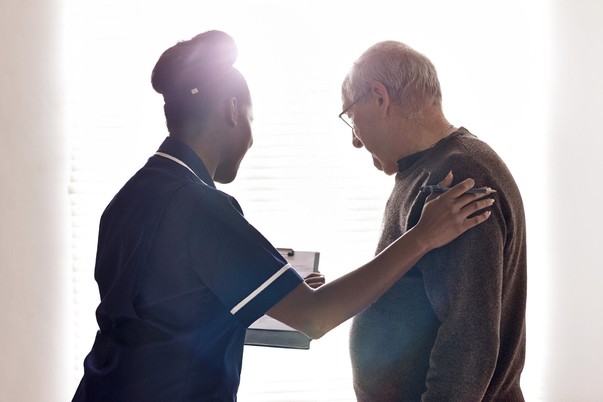A female caregiver comforts an older man.