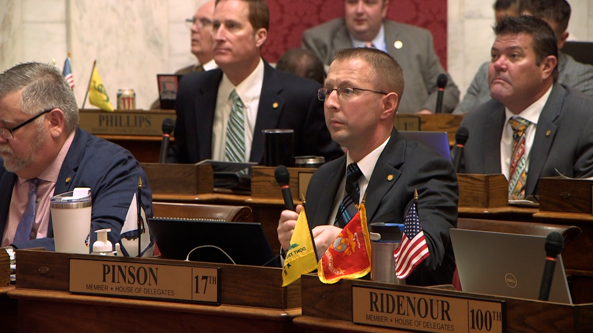 Crew cut delegate with flags at his desk listens to bills read.