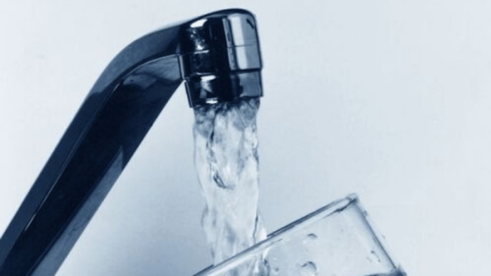 Water pouring from a faucet into a clear glass cup.
