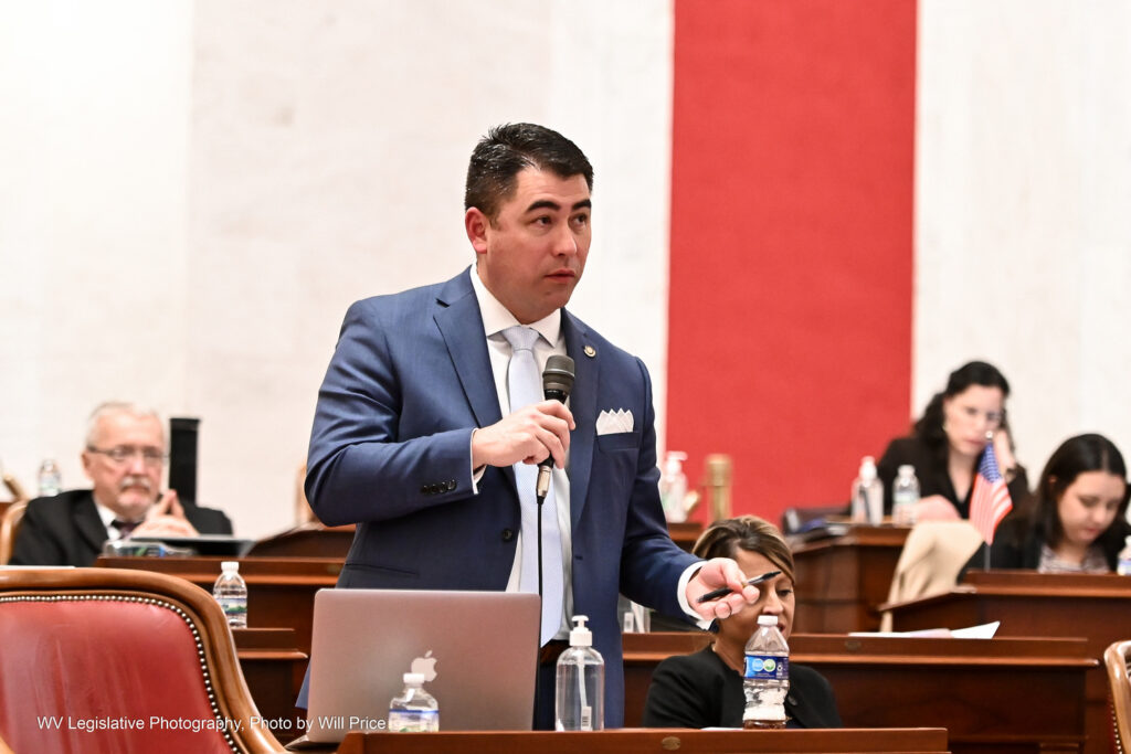 Senate Majority Leader Sen. Tom Takubo, R-Kanawha, speaks on the Senate floor Friday night, March 10, 2023. He wears a blue jacket over a white shirt with a light blue tie. In one hand he holds a microphone while gesturing with his other hand, which holds a pen.