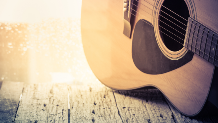 A close up of an acoustic guitar is shown on a porch or table.