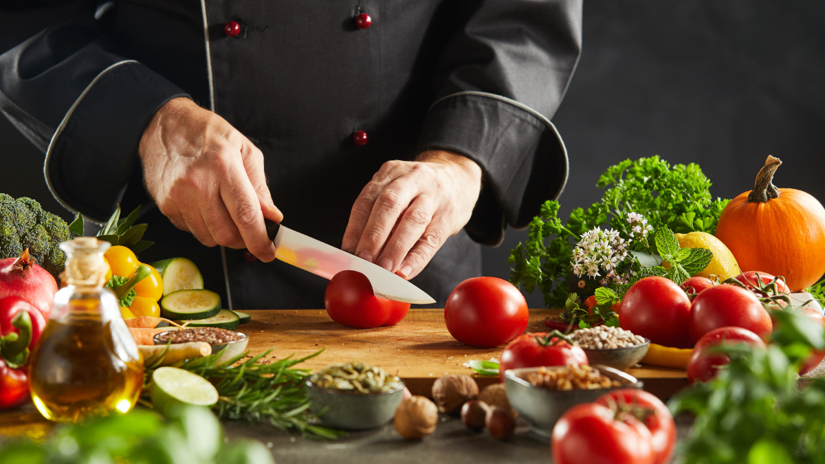A chef in a black apron cuts colorful vegetables on a cutting board.