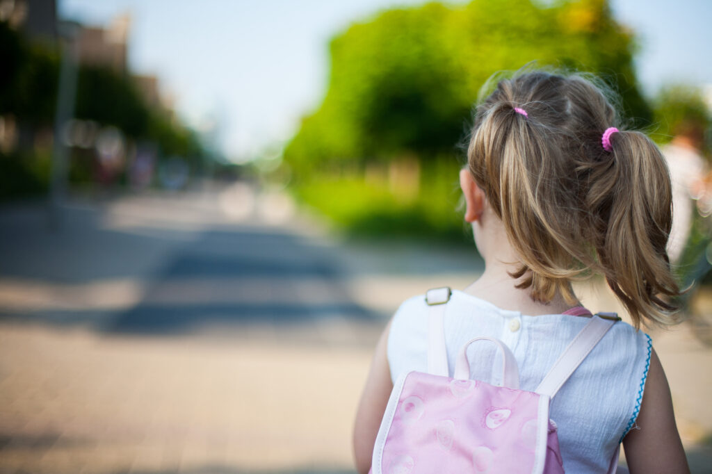 A child with pigtails and a pink backpack is seen walking down a road.