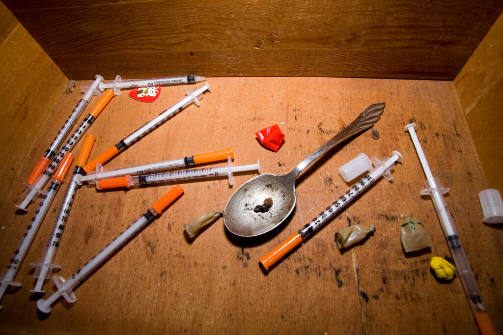 Drug paraphernalia with needles and a spoon are seen from above.