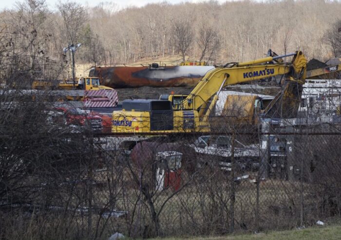 A burned up railroad tank car is seen behind a yellow piece of construction equipment in East Palestine, Ohio.