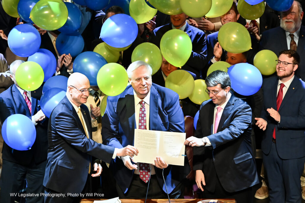 Three men hold a signed piece of legislation as balloons fall in celebration.