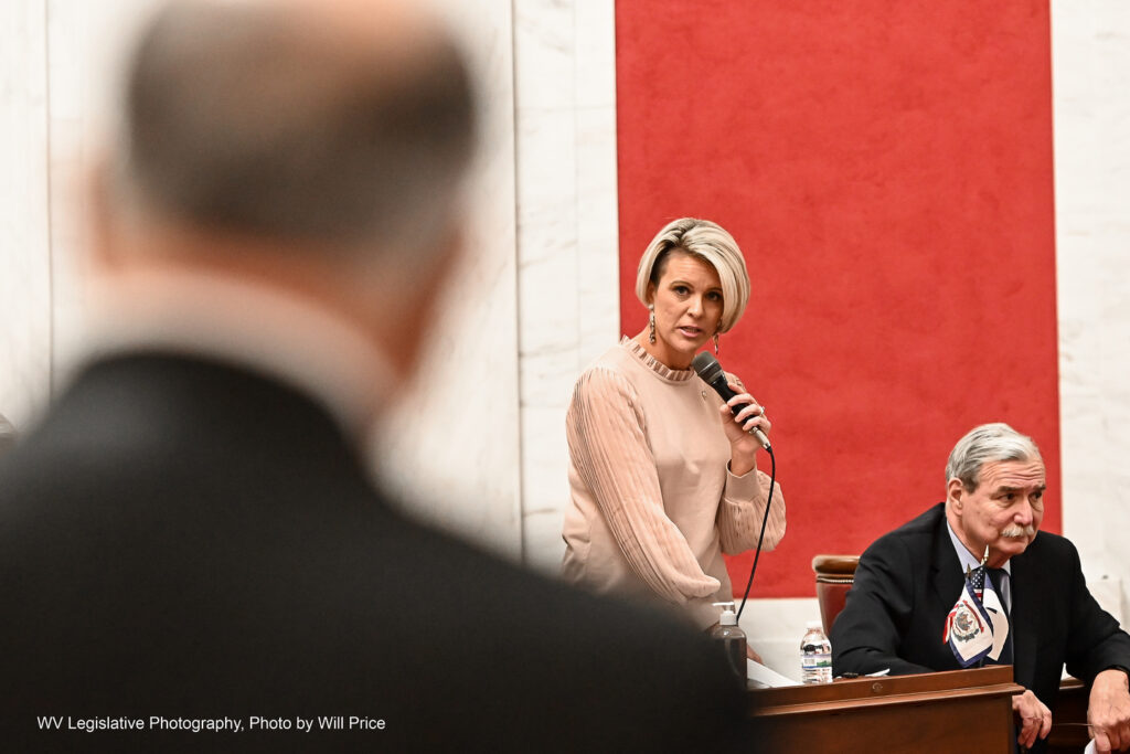 Blonde woman speaks into a microphone explaining a bill on the Senate Floor.