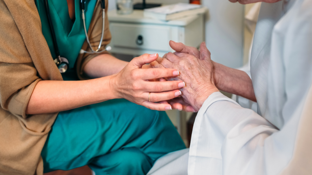 A close up on a doctor and an older patient holding hands in a comforting manner.