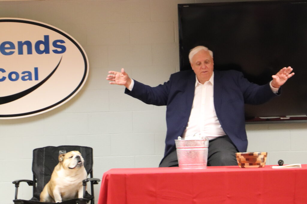 Gov. Jim Justice spreads his arms before signing bills at the John Amos power plant, with his English bulldog, Babydog, sitting in a chair next to him.