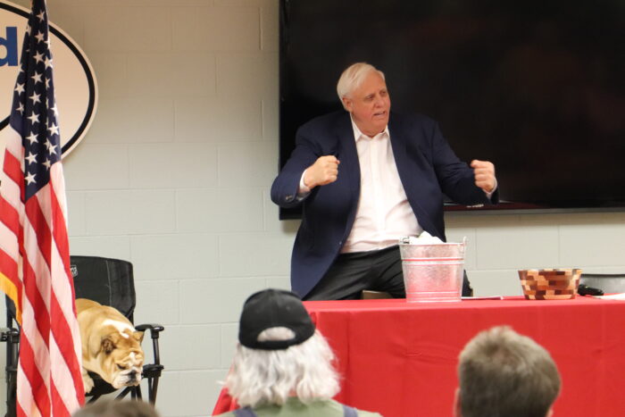 Gov. Jim Justice clenches his fists before signing bills at the John Amos power plant, with his English bulldog, Babydog, sitting in a chair next to him.