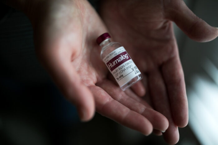 Two hands are shown holding a small vial of medicine.