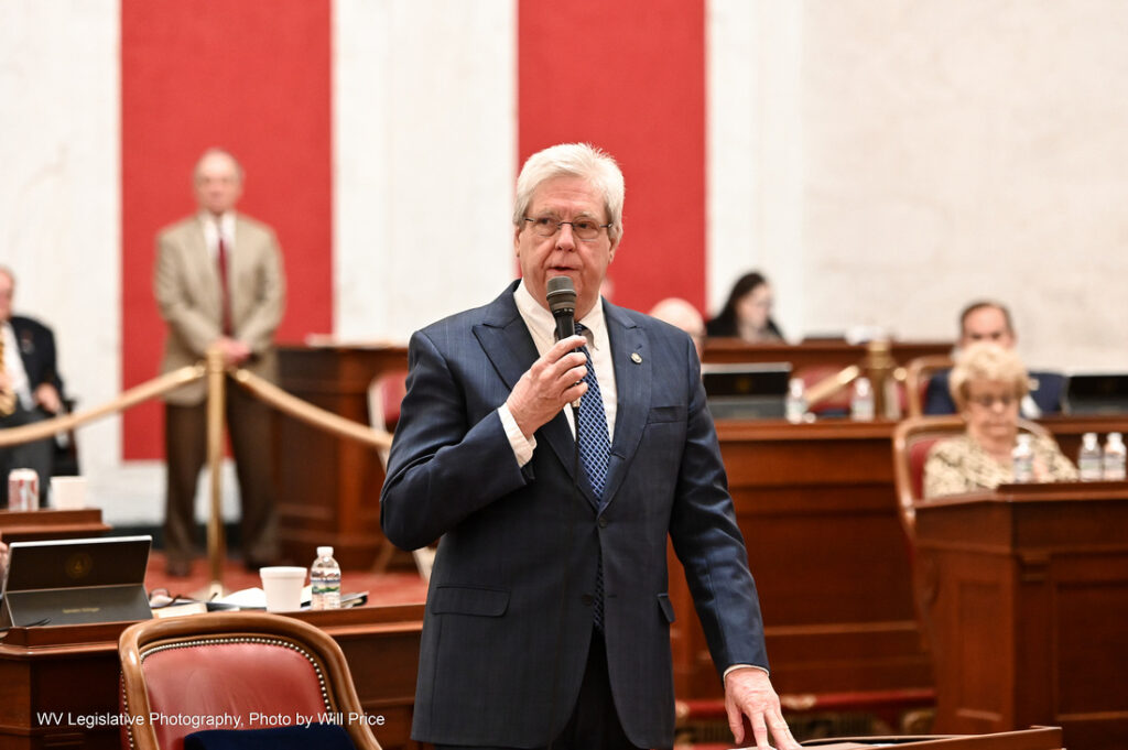 A man in a suit with grey hair and wearing glasses speaks into a microphone on the West Virginia Senate floor.