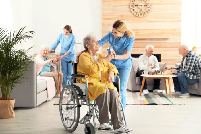 Nurse giving glass of water to elderly woman in wheelchair.
