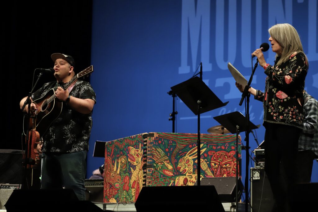 Two people stand on stage singing and playing an instrument.