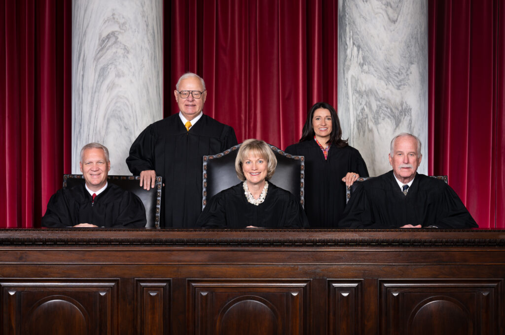 Five judges sit and stand at the bench. There are three men and two women.