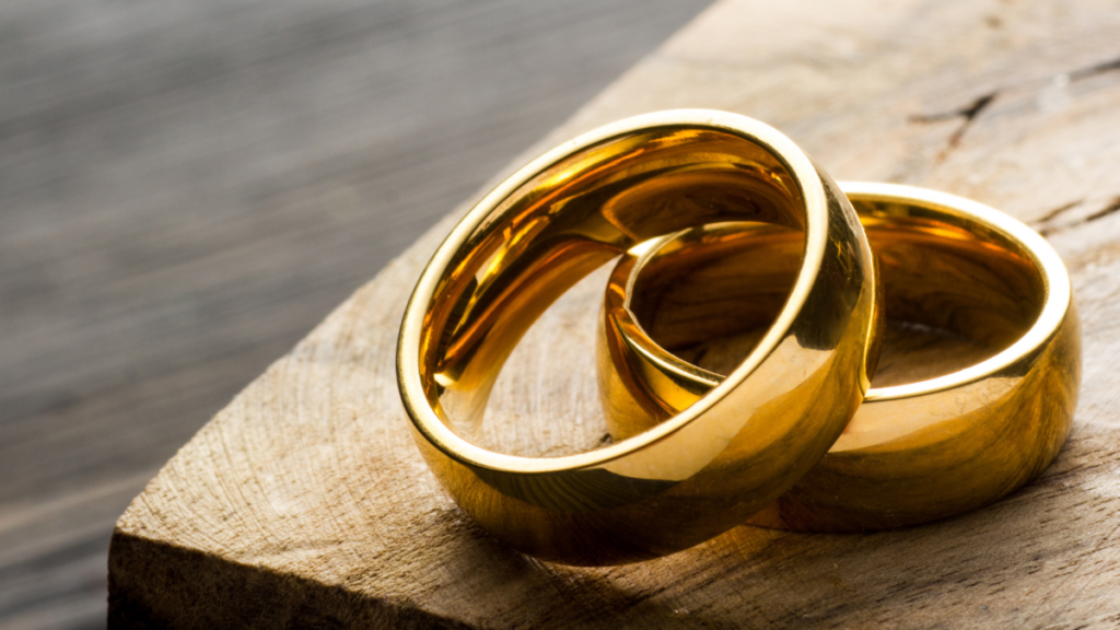 Two wedding rings are shown leaning against the other on a table.