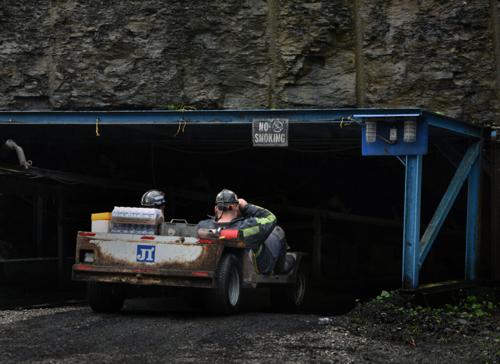 Two coal miners ride a mantrip cart into a mine.