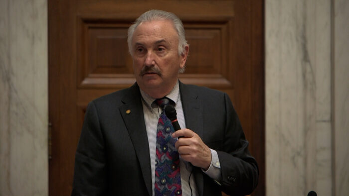 Gray haired man with moustache speaks on the House chamber floor.