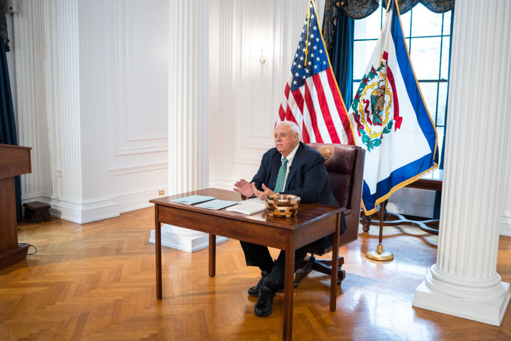 Gov. Jim Justice sitting at his desk wearing a green tie in honor of St. Patrick’s Day as he signs into law the state’s budget bill HB 2024 on Friday, March 17, 2023.