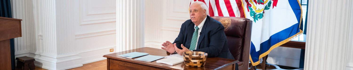 Gov. Jim Justice sitting at his desk wearing a green tie in honor of St. Patrick’s Day as he signs into law the state’s budget bill HB 2024 on Friday, March 17, 2023.