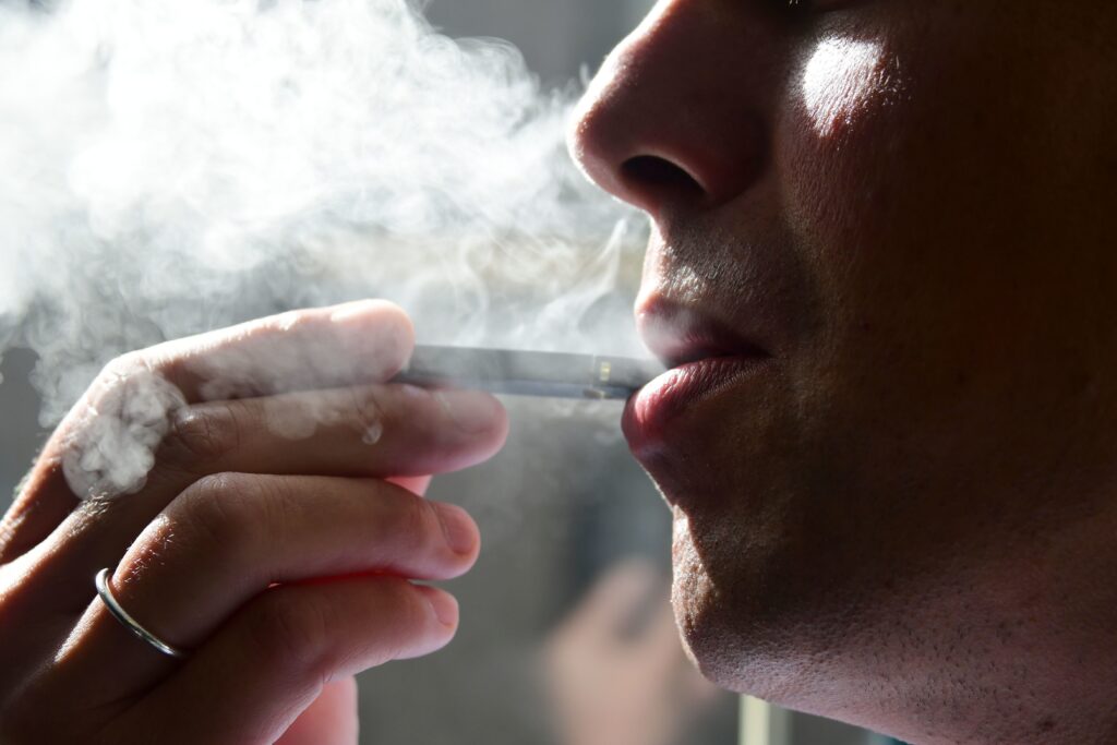 A man is seen from his left side smoking an electronic cigarette.