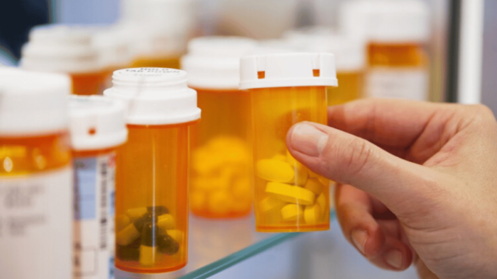 Hand grabbing bottle of opioid pills from pharmacy shelf