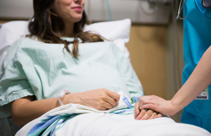 A patient lays in a hospital bed, smiling up and holding hands with a supportive physician.