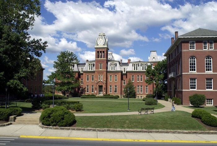 A large brick building with a prominent clock tower in the middle stands at the end of a large, green lawn.
