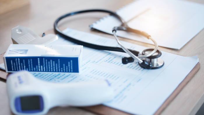 A thermometer and stethoscope are seen lying on top of a clipboard.