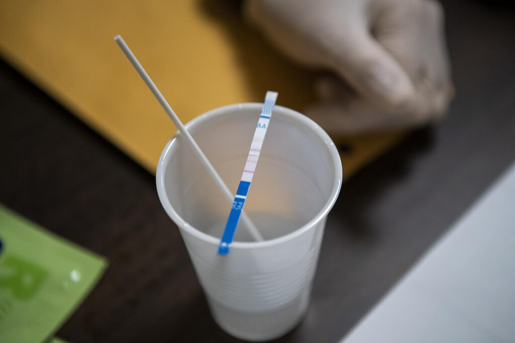 A drug testing kit is seen on a table with a cup of sample.