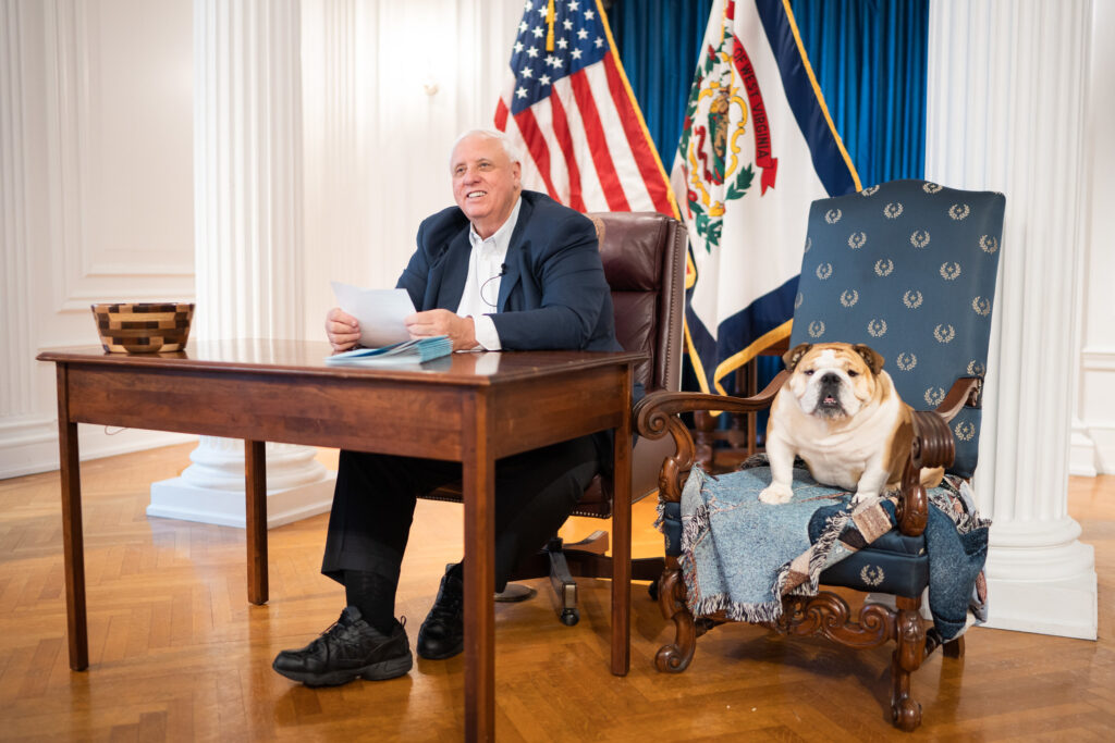 Man seated behind a small table with a bulldog in a chair beside him.