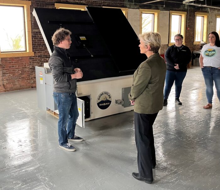 Two people speak to each other face to face inside an industrial building with bare brick walls and painted wood floors.