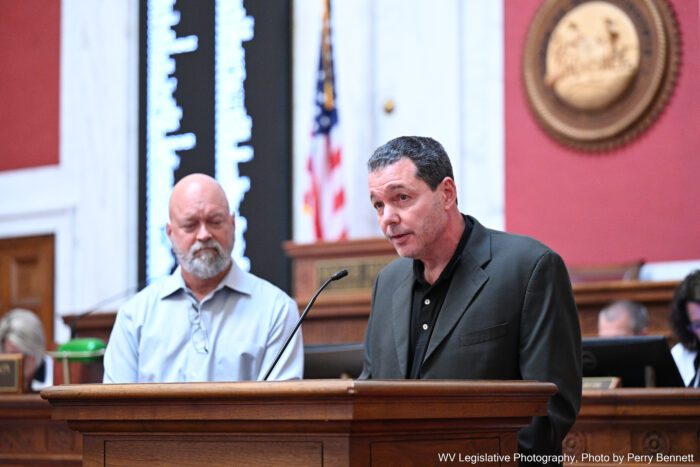 Two men are standing at a podium as one of them speaks into the microphone in a House of Delegates.